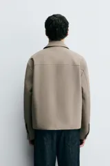 Sobrecamisa color beige de corte cuadrado, con cuello solapa, manga larga con puños abotonados, bolsillos laterales y cierre frontal con botones.