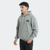 Canguro con capucha y cordones ajustables, color verde grisáceo. Presenta un bolsillo frontal tipo canguro y un parche bordado en el pecho con diseño de marca. Posee puños y ruedo acanalados.