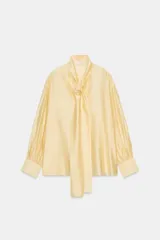 Camisa de corte holgado confeccionada en tejido satinado con mezcla de lyocell. Presenta cuello redondo con escote en pico y lazada frontal integrada. Cuenta con mangas largas abullonadas terminadas en puños anchos y bajo recto.