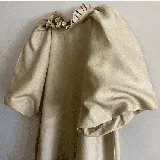 Vestido corto blanco de lino, con cuello redondo con detalle de fruncido y mangas cortas abullonadas. El calce es holgado tipo evasé con un pequeño volante en el ruedo.