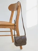 Cartera tipo mini bag de cuero con textura de reptil, color marrón, con solapa frontal y correa larga ajustable para usar al hombro o cruzada.