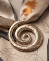 Pañuelo de seda con estampado de hojas y flores en tonos naranjas y grises sobre fondo beige, con bordes oscuros e incluye un dije dorado en forma de espiral.