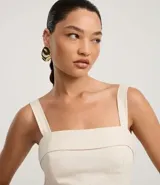 Vestido midi de corte evasé, color crema, con escote cuadrado y breteles anchos. Presenta un estampado grande de hojas y follaje en tonos oscuros en el ruedo inferior.