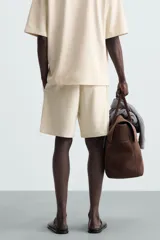 Bermuda de hombre color verde claro, de corte regular y tiro medio, con pinzas frontales, bolsillos laterales y bolsillos traseros de vivo. Cierre frontal con botón y cremallera.