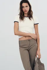 Pantalón capri de tiro medio con raya diplomática en tonos beige y marrón. Presenta trabillas, bolsillos laterales y cierre frontal con cremallera y botón metálico.