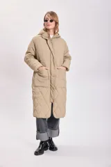 Campera color beige con capucha, cierre frontal con cremallera y broches a presión, bolsillos laterales y diseño acolchado con patrón de rombos.