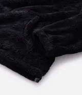 Buzo de tejido peludo color negro, con cuello alto y cierre frontal parcial. Presenta mangas largas con puños elásticos, bolsillo tipo canguro y etiqueta decorativa en el pecho.