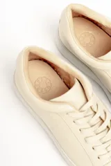 Zapatillas color beige claro, con capellada de cuero suave y acolchado, forro y plantilla de cuero vacuno, y suela de EVA. Tienen una plataforma de 3.8 cm en la parte trasera y 3.2 cm en la delantera.