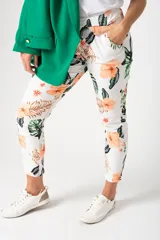 Babucha de corte relajado con estampado tropical de flores y hojas en tonos naranja y verde sobre fondo blanco. Presenta cintura elástica y bolsillos laterales.