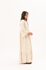 Vestido largo beige de silueta oversize, confeccionado en tela ligera con textura y motivos bordados tono sobre tono. Presenta escote en V, mangas amplias con volados y un gran volado en el ruedo.