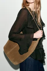 Bolso tipo saca de diseño asimétrico confeccionado en piel de ante. Cuenta con un asa bandolera ajustable, cierre mediante imán y un bolsillo interior con cremallera.