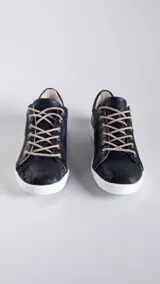 Championes de cuero negro jaspeado con suela blanca y cordones beige, con detalles pintados a mano en el talón y aplique metálico triangular.