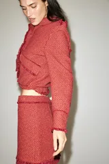 Chaqueta corta de tweed en color rojo, con cuello solapa, manga larga y bolsillos frontales con solapa. Presenta detalles deshilachados en los bordes y cierre frontal con cremallera oculta.