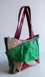 Cartera tipo tote de cuero combinada con diseño patchwork en tonos verde, bordó, beige y detalles metalizados, con doble asa de hombro y cierre superior.