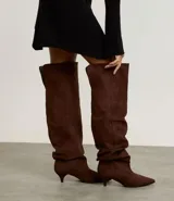 Bota over the knee color marrón, con acabado efecto gamuza y caída fruncida a lo largo de la caña. Presenta punta fina y tacón bajo y fino de 5 cm.