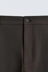 Pantalón de corte relajado con pliegues frontales, bolsillos laterales y bolsillos traseros de vivo. Presenta cierre frontal con cremallera y botón.