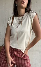 Remera sin mangas de color manteca, con detalle de tachas metálicas doradas en los hombros.