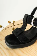 Sandalias de gamuza negra con taco cuadrado y plataforma. Presentan un diseño de tiras anchas con una hebilla metálica plateada ajustable en el lateral.