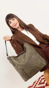 Cartera de hombro tipo hobo en color negro, confeccionada en material símil cuero con textura granulada. Presenta un diseño funcional con cierre principal, bolsillo frontal con cierre y detalles de tachas metálicas, además de una correa de hombro fija y una correa larga ajustable y extraíble.