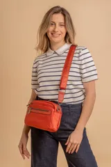 Bandolera de diseño moderno y funcional, confeccionada en nylon color marrón claro. Cuenta con múltiples compartimentos con cierre metálico, herrajes plateados y una correa ancha ajustable con detalle de marca.