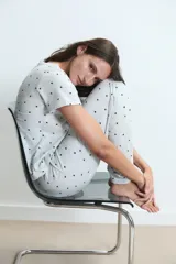 Pijama de dos piezas compuesto por una remera de manga corta y un pantalón largo, confeccionado en tejido de algodón gris claro con estampado de pequeños corazones negros.