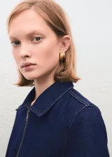 Mono de denim azul oscuro con cierre frontal de cremallera, cuello camisero y mangas cortas. Presenta un corte recto, bolsillos de parche delanteros y traseros, y un cinturón de la misma tela para ajustar la cintura.