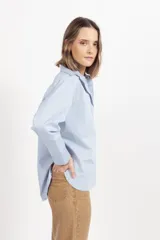 Camisa de corte clásico y diseño holgado, color celeste, con cuello camisero, cierre frontal de botones y mangas largas con puños abotonados.