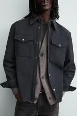 Sobrecamisa de corte relajado confeccionada en tejido efecto piel color marrón oscuro. Presenta cuello solapa, cierre frontal con botones metálicos, mangas largas con puños abotonados y dos bolsillos de plastrón con solapa en el pecho.