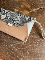 Sobre de cuero color naranja con estampado animal print, forrado y con bolsillo interior con cierre. Incluye pulsera desmontable.