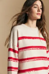 Sweater de punto con diseño de rayas horizontales en color rojo sobre base color crema. Presenta un efecto visual texturizado en las franjas rojas, cuello redondo y mangas largas con silueta relajada.