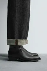 Bota corta negra estilo cowboy, con caña lisa, punta cuadrada y tirador trasero. Ajuste mediante cremallera lateral y tacón bajo.