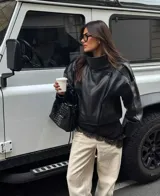 Chaqueta de cuero sintético color negro con acabado granulado, diseño oversize, cuello alto estructurado y cierre asimétrico.