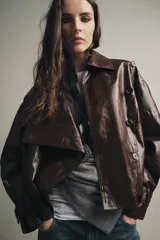 Chaqueta de Zara Woman Collection en tejido con acabado brillante efecto cuero. Presenta cuello solapa, manga larga con trabillas ajustables, bolsillos delanteros y cierre frontal con botones ocultos bajo solapa.