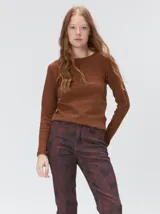 Remera de manga larga con cuello a la base, confeccionada en tejido de punto acanalado color beige. Presenta un logo bordado en el centro del pecho.