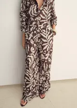 Pantalon de corte recto y tiro medio, con cintura elástica y cordón ajustable. Presenta un estampado abstracto de hojas en tonos marrones y crema, y cuenta con dos bolsillos laterales.