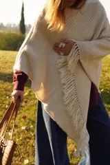 Poncho tejido en lana merino color marrón, con diseño de punto acanalado y terminación con flecos en el borde inferior. Incluye una pequeña etiqueta de cuero en la parte posterior.