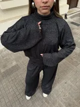 Conjunto de dos piezas compuesto por un buzo de cuello alto y mangas largas con diseño holgado, y un pantalón a juego. Ambas prendas están confeccionadas en tejido morley elastizado de color negro con un sutil efecto jaspeado.