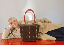 Cartera tipo tote de gamuza color marrón, con correas trenzadas y detalle de piedras naturales incrustadas en líneas verticales. Cuenta con cierre metálico y forro interior de tela.