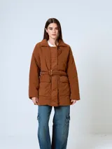 Campera de pana color marrón, con diseño acolchado, cuello camisero, cierre frontal oculto y cinturón ajustable con hebilla a tono. Presenta bolsillos frontales con solapa y mangas largas de corte holgado.