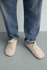 Zapatilla de cordones para hombre, confeccionada en piel con acabado de serraje en color beige. Presenta un diseño de perfil bajo con detalles de pespuntes decorativos y una suela ultrafina.