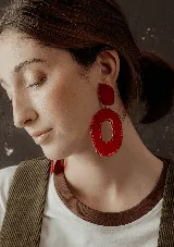 Aros colgantes con forma geométrica irregular, color rojo. El aro superior es pequeño y redondeado, mientras que el aro inferior es grande y con un agujero en el centro.