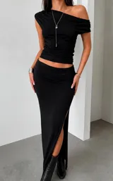 Conjunto de dos piezas compuesto por un top de un solo hombro con diseño drapeado y una falda larga de tiro bajo con tajo lateral profundo.