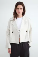 Campera estilo trench corta color beige, con solapas amplias, cierre cruzado de doble botonadura con botones oscuros y diseño holgado.