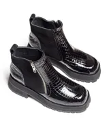 Botas cortas negras con plataforma dentada, confeccionadas en una combinación de cuero con textura de reptil y paneles de gamuza. Presentan un cierre frontal metálico y puntera cuadrada.