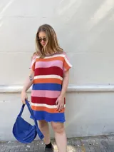 Vestido corto tejido a rayas horizontales en tonos crudo, naranja, rojo, rosa, azul y blanco.