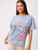 Remera celeste de corte holgado, con cuello redondo, manga corta y estampado frontal colorido de temática costera.
