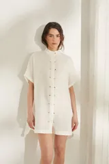 Vestido corto color beige de lino, con moldería amplia, manga corta, cuello mao y cierre frontal con botones dorados.