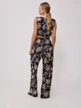 Pantalon de corte recto y holgado, confeccionado en algodón estampado con motivos playeros como palmeras, soles y caracoles en color crema sobre fondo negro. Posee cintura elástica.