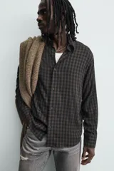 Camisa de corte relajado con diseño de cuadros en tonos negro y beige, cuello camisero, manga larga y cierre frontal de botones.