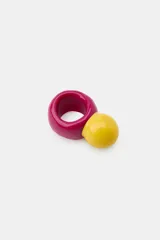 Pack de dos anillos de resina multicolor. Uno de los anillos presenta un diseño liso en color fucsia con una aplicación esférica amarilla en contraste, mientras que el otro cuenta con una base blanca y un aplique en relieve con forma de flor en tonos azul y blanco.